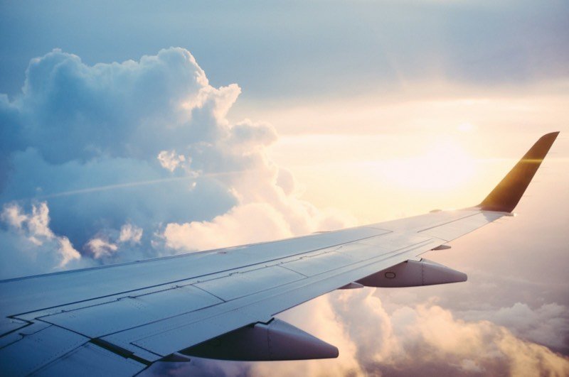 Airplane wing above sunlit clouds